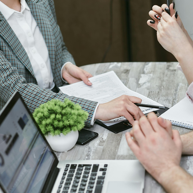 business-woman-sitting-at-table-reviewing-paperwork-with-couple Business Woman sitting across from a couple holding a pen and pointing to papers